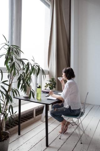 picture of person on laptop looking out window with teacup in hands 