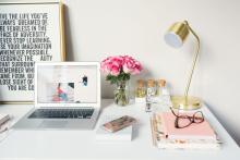 picture of a laptop on a white desk with a motivational poster and a jar of roses