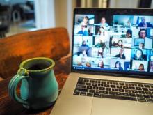 image of a laptop with a gallery view of a zoom meeting and cup of coffee next to computer