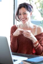 image of woman with a cup of coffee smiling in front of a computer screen