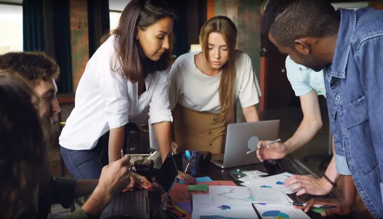 picture of a team working around a table looking down at table with scattered papers 