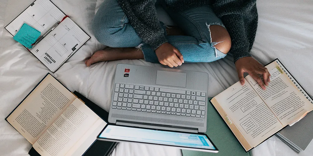 picture of person sitting on a bed surrounded by books and resource materials