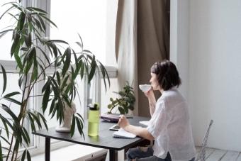 picture of person on laptop looking out window with teacup in hands 