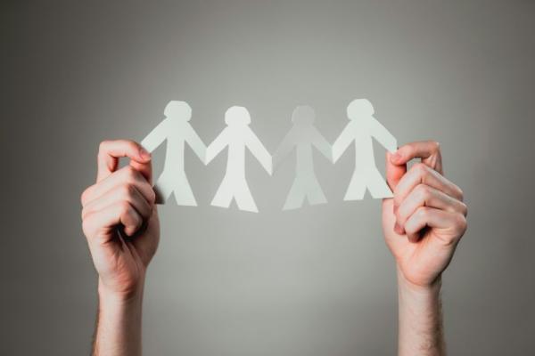 picture of a pair of hands holding a paper cutout of people holding hands