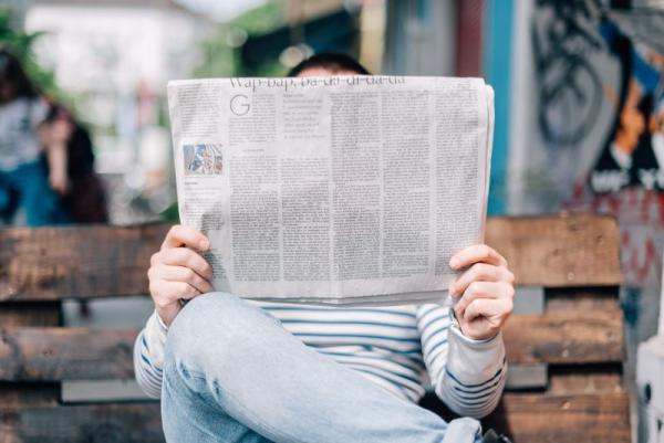 picture of a person reading a newspaper in front of their face while sitting on a bench outside