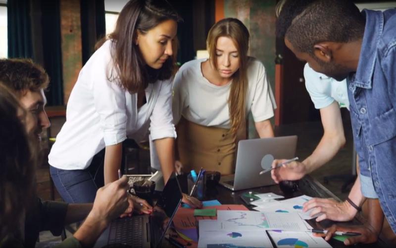 picture of a team working around a table looking down at table with scattered papers 