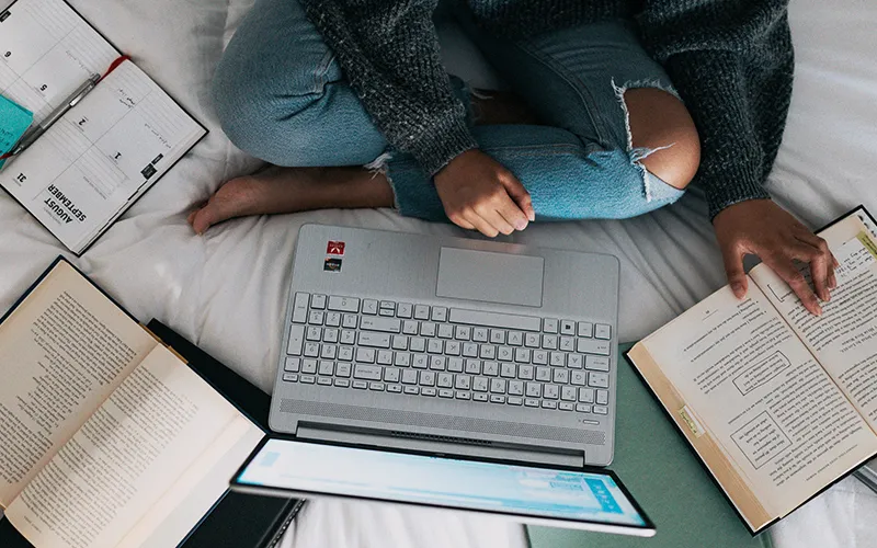 picture of person sitting on a bed surrounded by books and resource materials